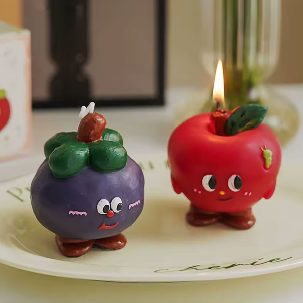 Two novelty fruit candles on a plate, one lit. An everyday object, chipped.
